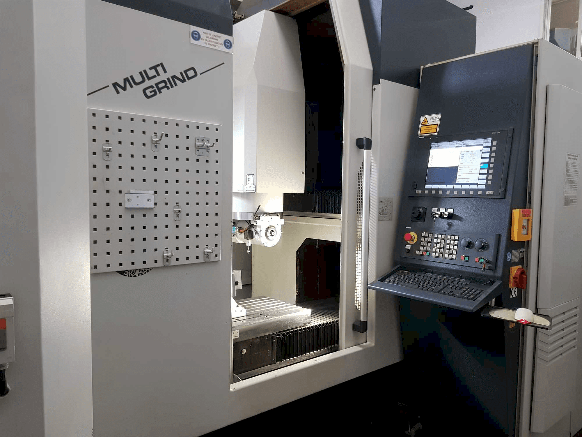 Macchina CNC Multi Grind con vista frontale, caratterizzata da un pannello di controllo, un pannello di stoccaggio e un'area di lavoro aperta.